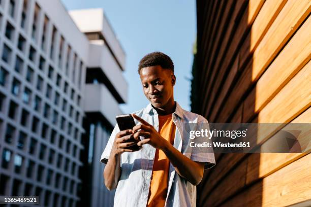 man using smart phone by orange wall in city - low angle view imagens e fotografias de stock