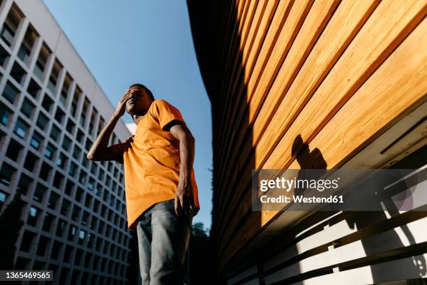 man rubbing eye with hand standing near wall on sunset - rubbing eyes stock pictures, royalty-free photos & images