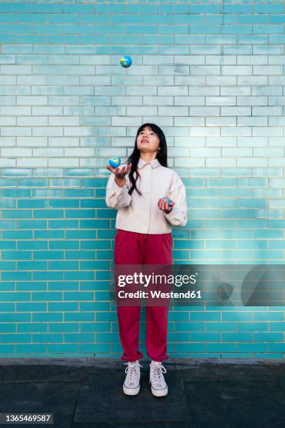 young woman juggling with small globes in front of turquoise brick wall - fare il giocoliere foto e immagini stock