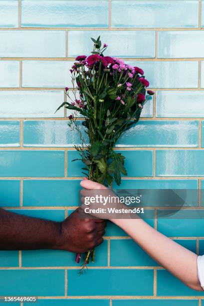 man and woman holding bouquet on turquoise brick wall - man giving flowers stock-fotos und bilder