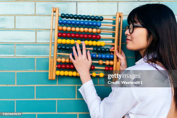 young woman counting beads on abacus by brick wall - abacus stock pictures, royalty-free photos & images