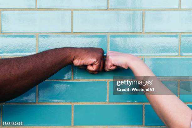 man and woman giving fist bump on turquoise brick wall - fist bump photos et images de collection