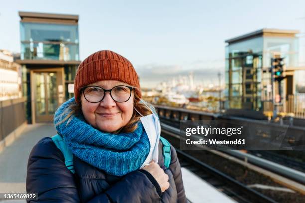 smiling senior woman taking off surgical mask at railroad station during pandemic - geschworener stock-fotos und bilder