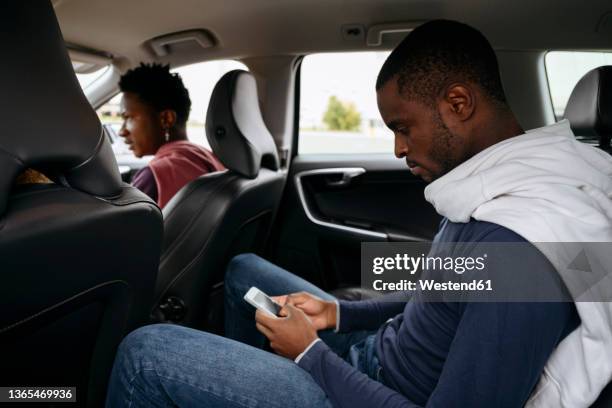 young man using smart phone with friends in car on road trip - 3 guy friends road trip stock-fotos und bilder