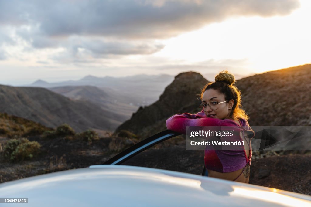 Woman leaning on car door with mountains in background
