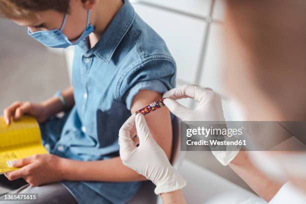 nurse putting adhesive bandage on boy's arm at vaccination center - impfung stock-fotos und bilder