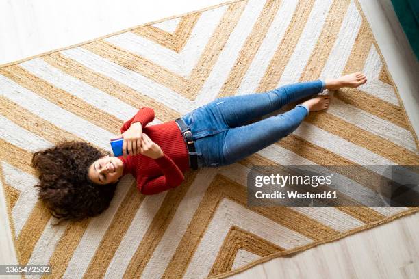 woman using smart phone lying on patterned carpet at home - supino foto e immagini stock