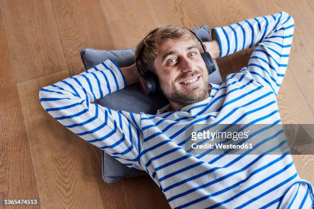 smiling man relaxing with hands behind head on cushion at home - einzelner mann über 30 stock-fotos und bilder