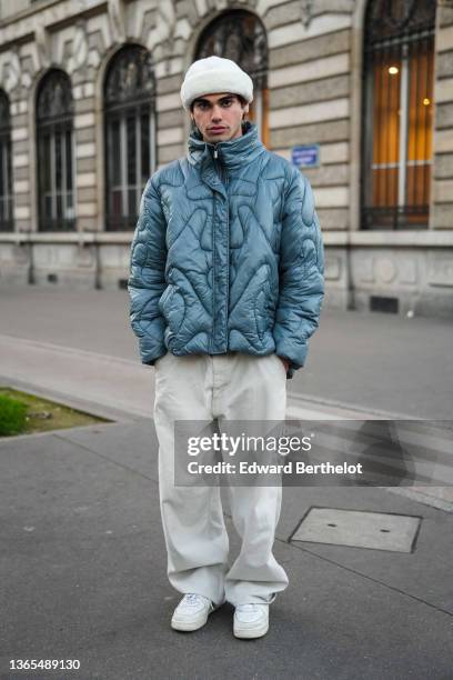 Guest wears a white beanie hat, a blue puffer jacket with geometric patterns, white large pants, white sneakers shoes, outside the Bluemarble show,...