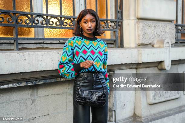 Guest wears large circular earrings, a blue yellow and red wool pullover with printed geometric patterns and puff sleeves, a black leather bag with...