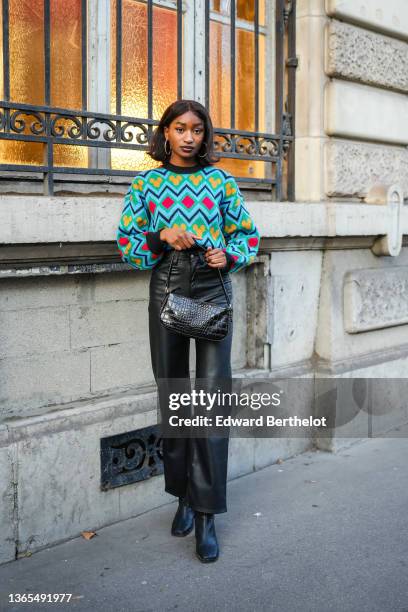 Guest wears large circular earrings, a blue yellow and red wool pullover with printed geometric patterns and puff sleeves, a black leather bag with...