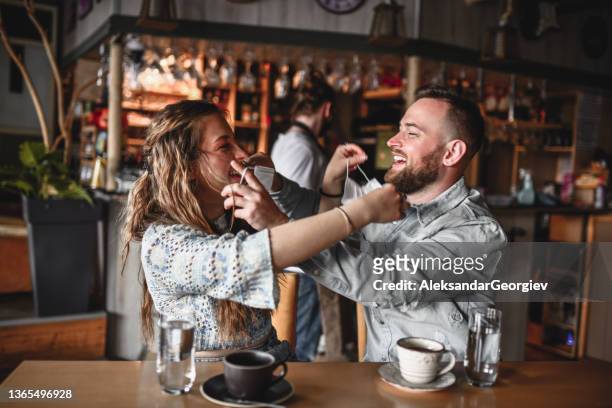 paar, das sich beim kaffeetrinken im restaurant gesichtsmasken auf die gesichter des anderen legt - couple in cafe man beard coffee stock-fotos und bilder