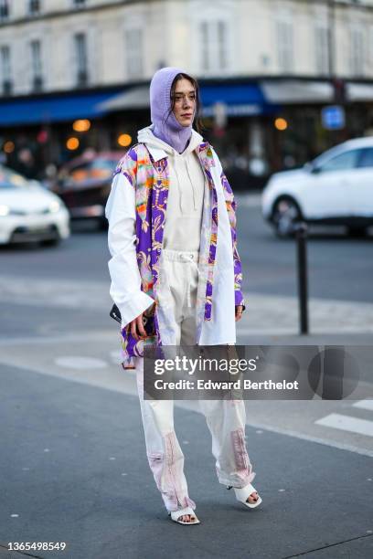 Maeva Marshall wears a pastel pale purple wool balaclava hood, a white hoodie sweater, a white shirt with white sleeves and purple printed patterns,...