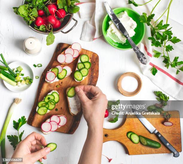 woman making a crostini with cream cheese, radishes and cucumber, top view. - immagine on white board foto e immagini stock