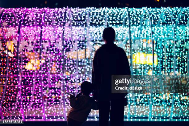 silhouette of mother holding hands of little daughter standing against illuminated and colourful bokeh lights background in the city at night - christmas celebrations in china imagens e fotografias de stock