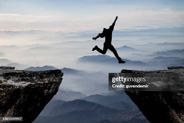 silhouette of man jumping from one cliff to another cliff with excitement - klif stockfoto's en -beelden
