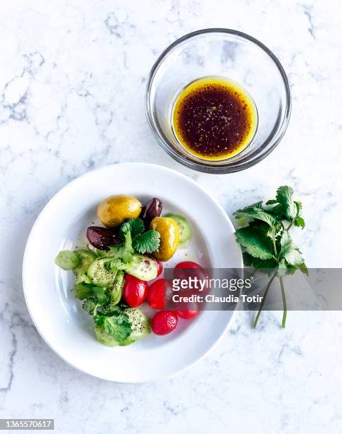 plate of side fresh salad with tomatoes, cucumber, and olives, and a bowl of vinaigrette on white, marble background - molho vinagrete imagens e fotografias de stock