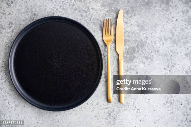 empty black ceramic plate and golden fork and knife on grey concrete background, top view - gold plate stock pictures, royalty-free photos & images