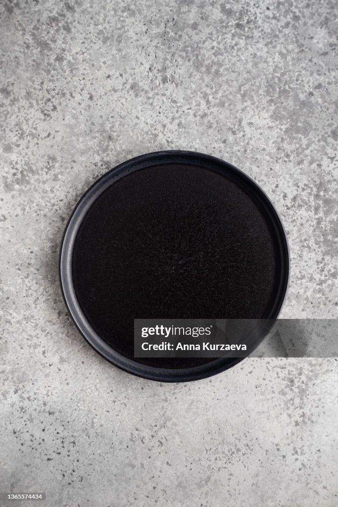 Empty black ceramic plate on grey concrete background, top view
