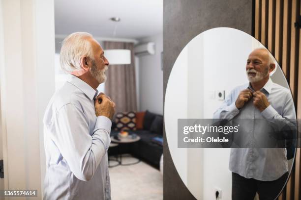 senior businessman getting ready for work - buttoning shirt stockfoto's en -beelden