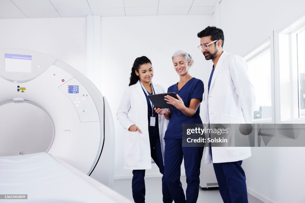 Three healthcare workers in conversation in CAT scanner room