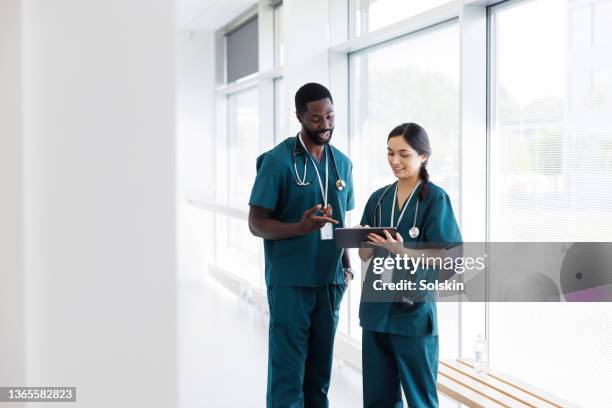 two doctors in hospital hallway discussing electronic  patient record - doctor stock photos et images de collection