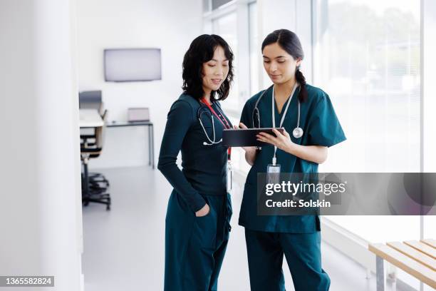 two female healthcare workers in hospital hallway, using digital tablet - medical research patient stock pictures, royalty-free photos & images