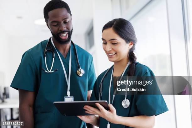 two doctors looking at digital tablet in hospital hallway - nurse - fotografias e filmes do acervo