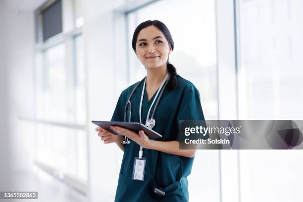 female doctor in hospital looking at digital tablet - trabajador-sanitario fotografías e imágenes de stock