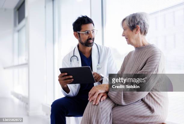 doctor and patient in conversation, looking at digital tablet - gezondheidszorg en medicijnen stockfoto's en -beelden
