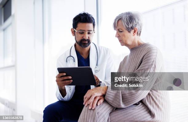 doctor and patient in conversation, looking at digital tablet - doctor and patient talking imagens e fotografias de stock
