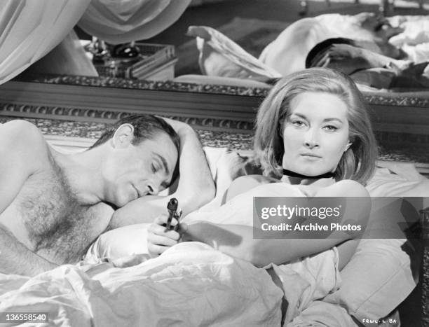 Sean Connery sleeping while Daniela Bianchi, next to him is sitting up pointing a gun in a scene from the film 'James Bond: From Russia With Love',...