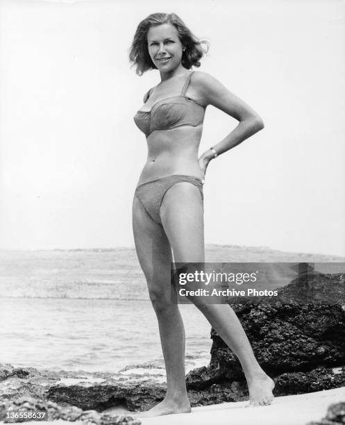 Honor Blackman standing on the beach wearing a bikini in a scene from the film 'Goldfinger', 1964.