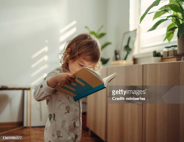 adorable young girl standing and reading the book in the morning - books stockfoto's en -beelden