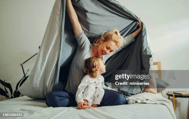 happy mother and daughter sitting on the bed under the sheets and playing - family cover stock pictures, royalty-free photos & images