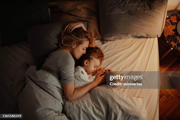 loving mother and daughter sleeping together in bed in the evening - family embracing stock pictures, royalty-free photos & images