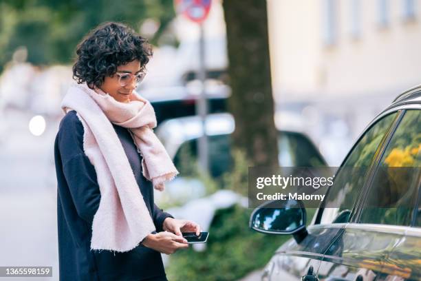 young woman unlocking her car with her phone. digital key with nfc, keyless, wallet or key fob - communication en champ proche photos et images de collection