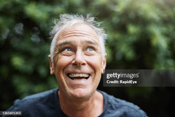 joyful handsome man in his 50s smiling and laughing happily outdoors in a garden - surprised face stockfoto's en -beelden