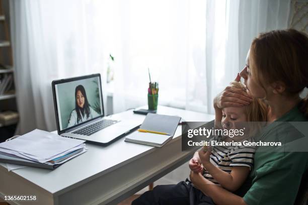 a young mother with a sick child consults a laptop with a doctor online from home. - telemedicine stock pictures, royalty-free photos & images