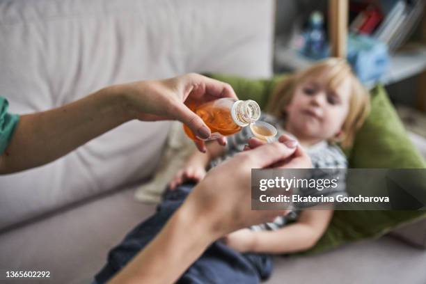 a young mother treats a child's cough at home, gives a spoonful of cough medicine. - syrup stockfoto's en -beelden