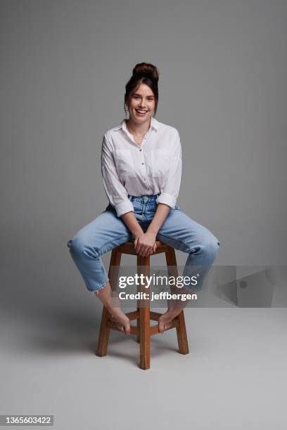 plan de studio d’une belle jeune femme assise sur une chaise sur fond gris - tabouret photos et images de collection