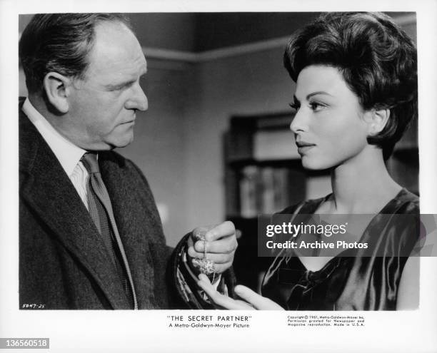 Haya Harareet accepting a piece of jewelry from actor Bernard Lee in a scene from the film 'The Secret Partner', 1961.