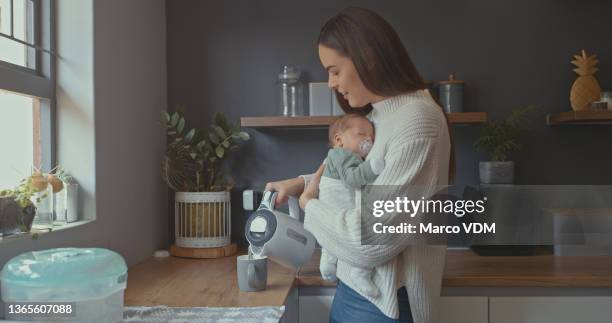 shot of a young woman pouring herself a cup of tea while holding her baby - baby cup spill stock pictures, royalty-free photos & images