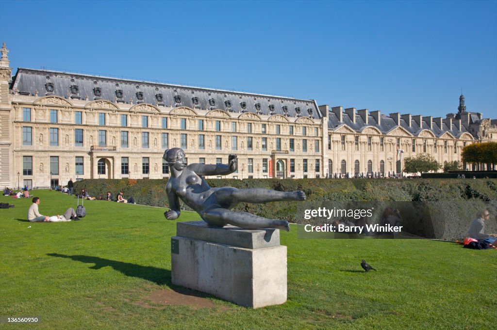 People relaxing on lawn near sculpture.