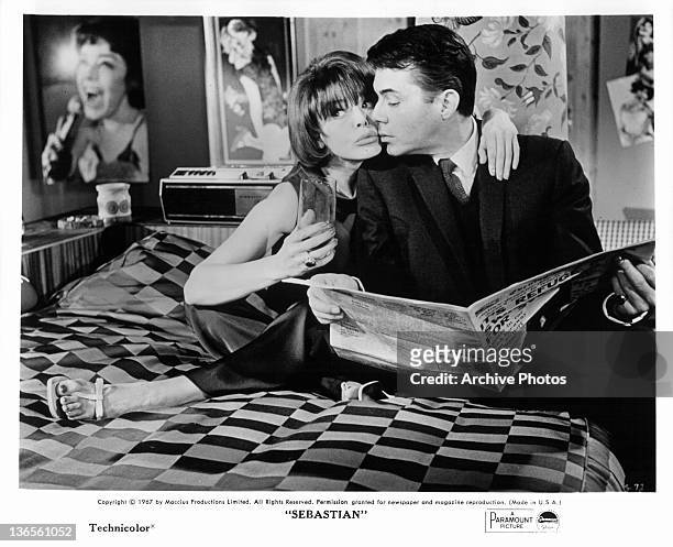 Dirk Bogarde sitting on a bed reading the newspaper with an Janet Munro in a scene from the film 'Sebastian', 1968.