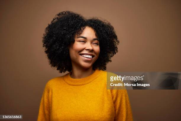 happy woman with curly hair against brown background - glimlach stockfoto's en -beelden