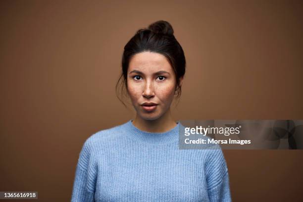 confident mixed race woman against brown background - expresiones de la cara fotografías e imágenes de stock