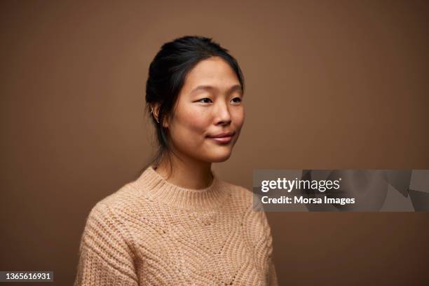 young woman in sweater against brown background - woman portrait side stock-fotos und bilder