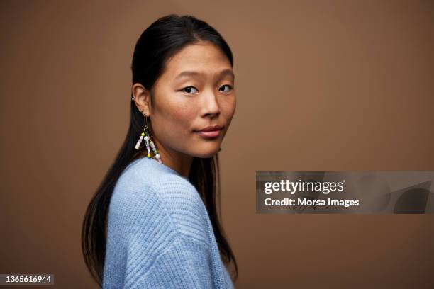 woman in blue sweater against brown background - woman looking over shoulder stock-fotos und bilder