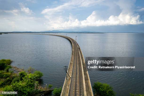 aerial view of thai local train on railway bridge at pa sak jolasid dam, the biggest reservoir in central thailand, in lopburi province with sea shore in transportation and travel concept. - biggest dam stock pictures, royalty-free photos & images